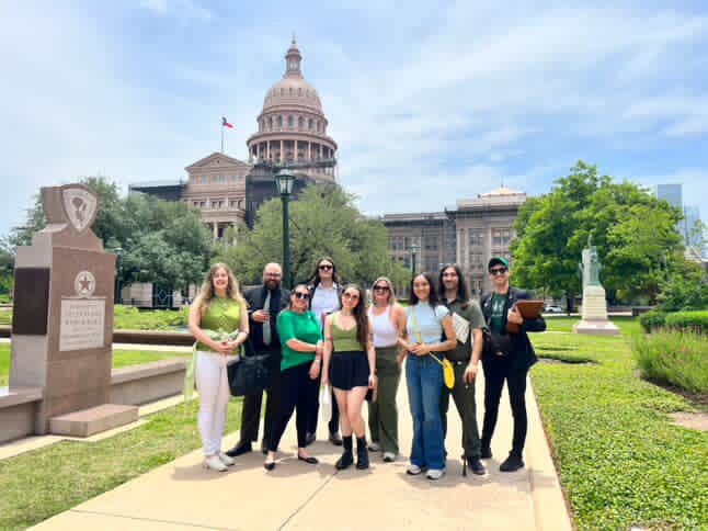 Nine advocates standing together on the Texas Capitol grounds, the dome behind them
